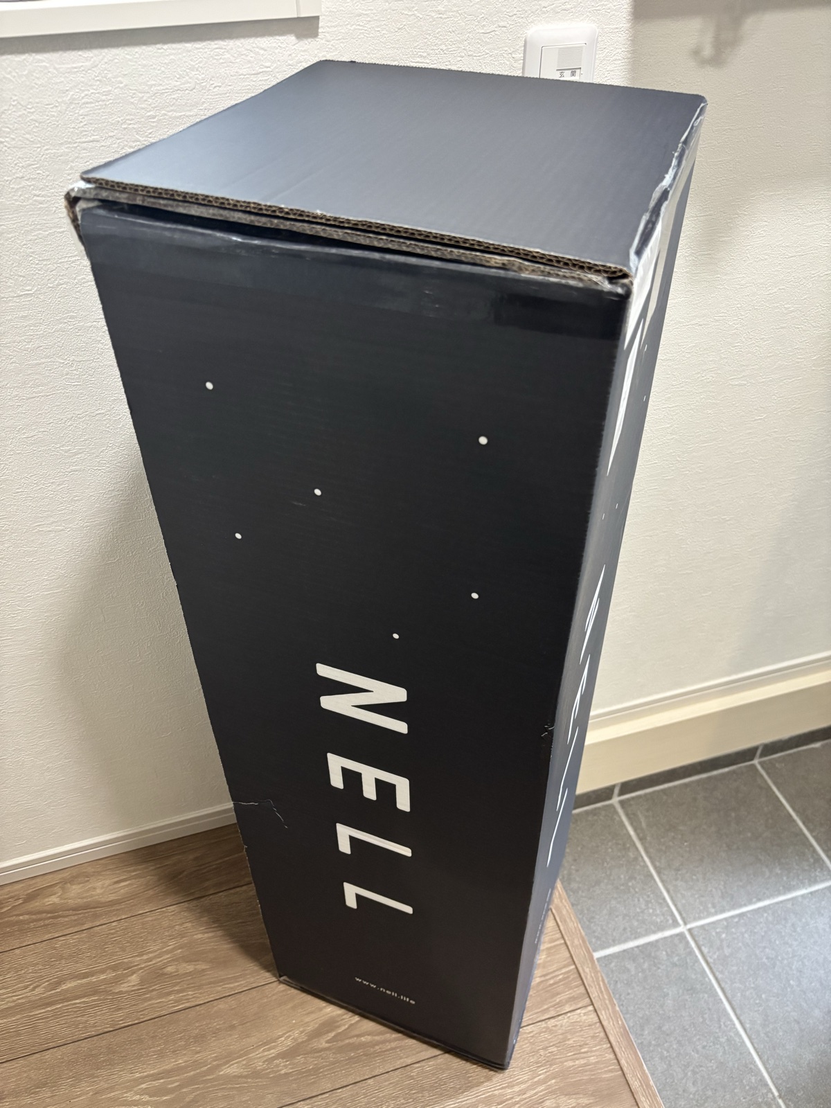 玄関付近に立てたNELLマットレスの黒い配送用段ボール箱